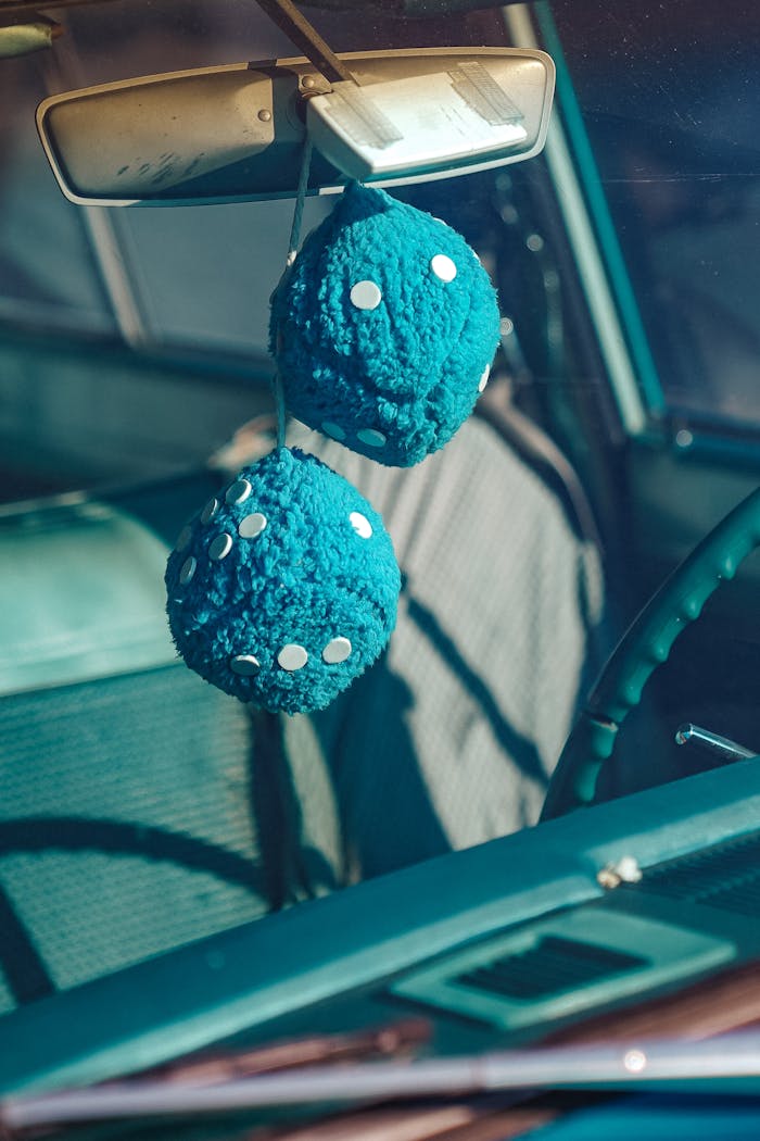 Close-up of a vintage car interior with blue fuzzy dice hanging from the mirror.