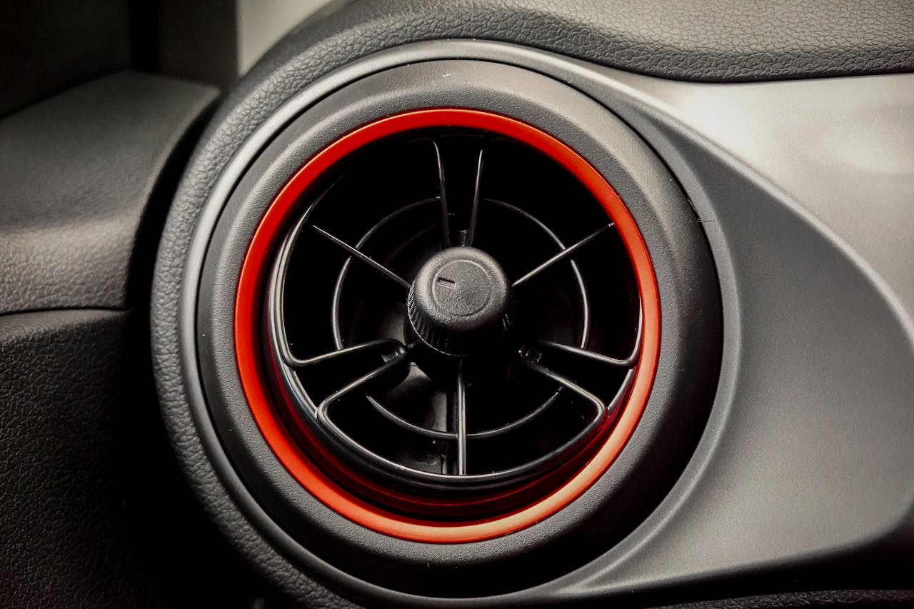 Close-up of a circular car air vent with stylish red trim. Ideal for automotive themes.